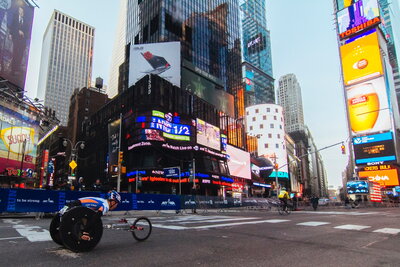 A man in a racing wheelchair racing through Times Square in New York City.